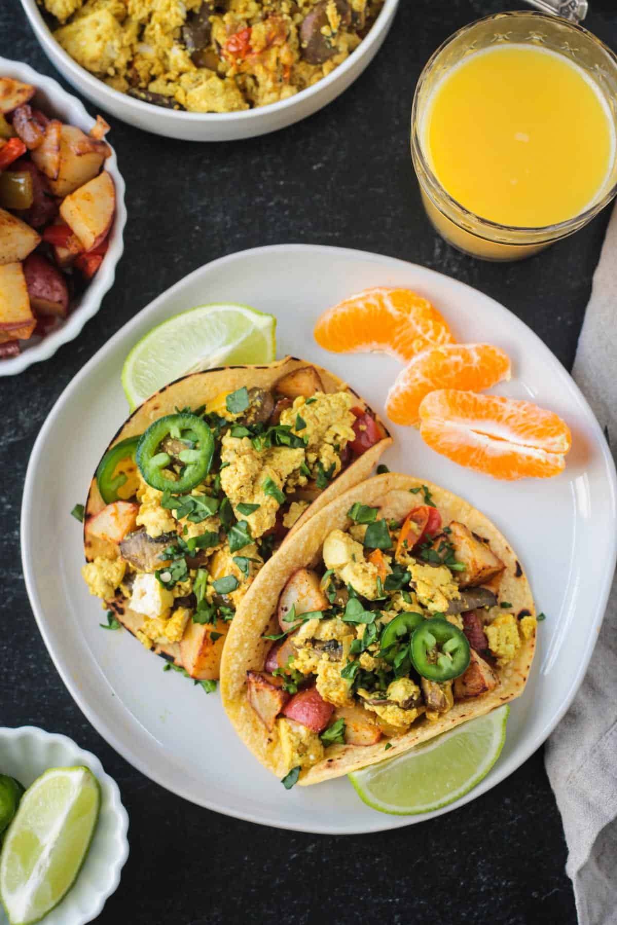 Healthy Breakfast Tacos w/ Scrambled Tofu & Roasted Potatoes. The flavors of the southwest are prominent in these delicious vegan tacos that are suitable for breakfast, lunch or dinner. Top them off with avocado, sliced jalapeño, salsa, and my very favorite Creamy Cumin Dairy Free Ranch Dressing! Overhead view of two corn tortillas filled with tofu, potatoes and peppers.