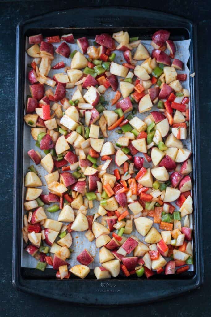 Diced raw potatoes and peppers on a sheet pan.