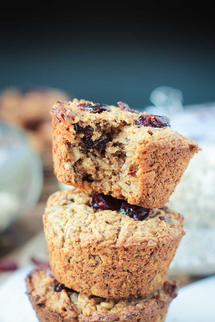 Baked Oatmeal Muffins w/ Cranberries - hearty and healthy, these delicious gluten free muffins will keep you satisfied all morning long. Perfectly portable if you're on-the-go. They make great lunchbox treats (they're nut free!) and after school snacks too! 3 stacked Cranberry Baked Oatmeal Muffins. Top muffin has a bite taken off.