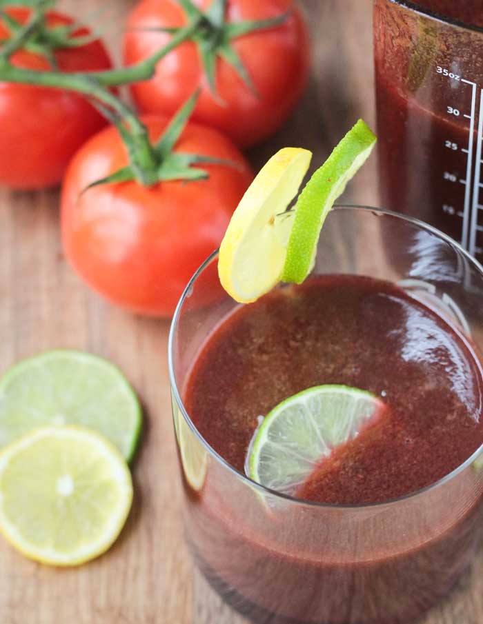 Spicy Tomato Juice - easy to make at home and YOU control the ingredients! No salt, no sugar, and you can make it as spicy or mild as you like. I've never liked tomato juice until this recipe!! Try it for yourself! And feel free to add some vodka to make it a Bloody Mary if you wish! Spicy Tomato Juice in a glass with a lime slice floating on top. One lime slice and one lemon slice on the edge of the glass.