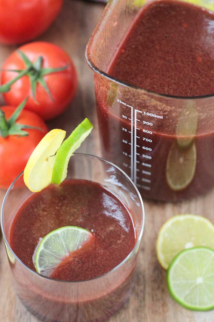 Spicy Tomato Juice in a glass. Lime and lemon slices next to the glass. Pitcher or more juice behind.