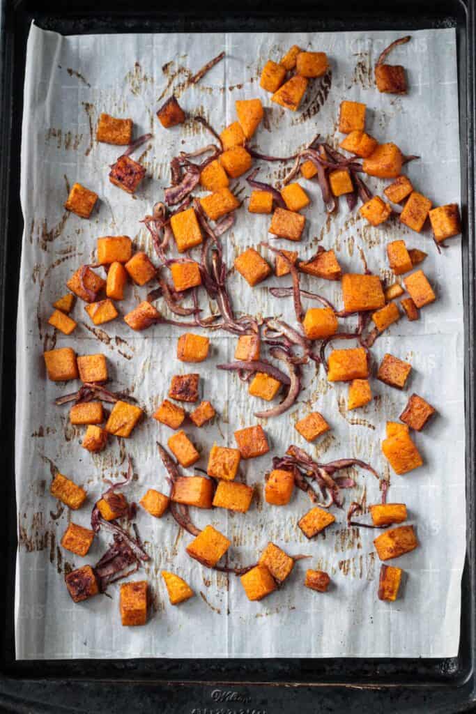 Roasted squash and red onions on a baking sheet.