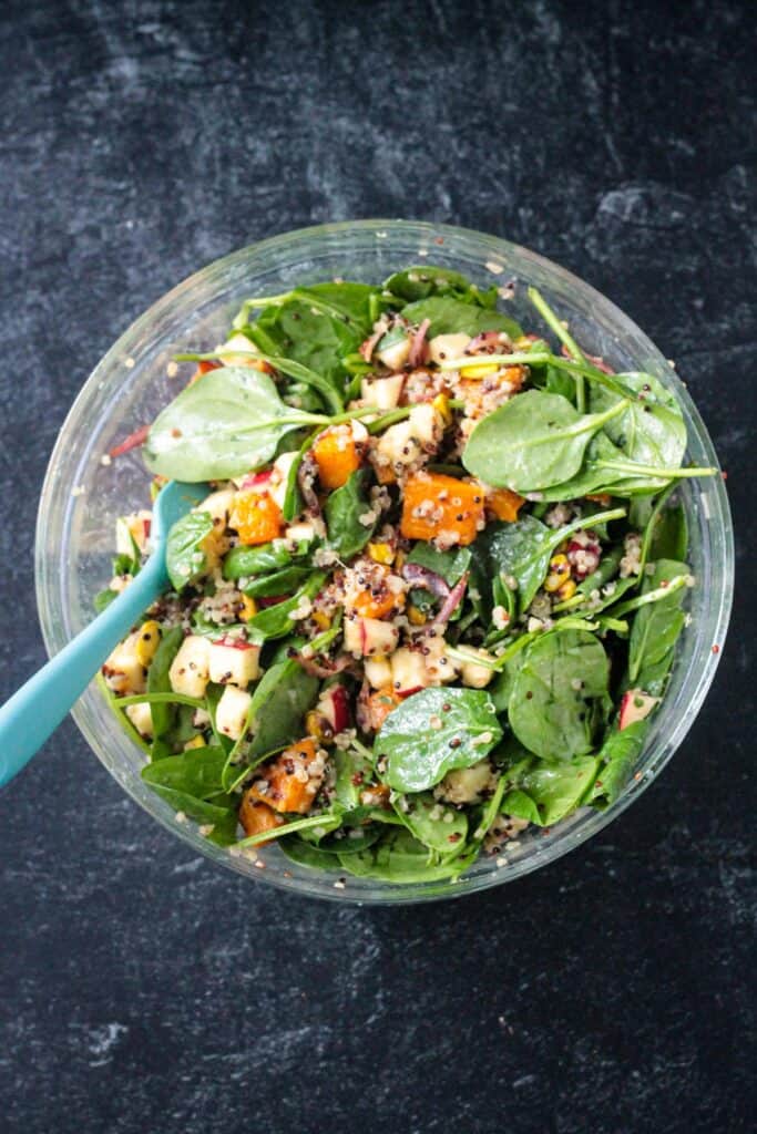 Cooked squash and onions added to the bowl of spinach and and apples.