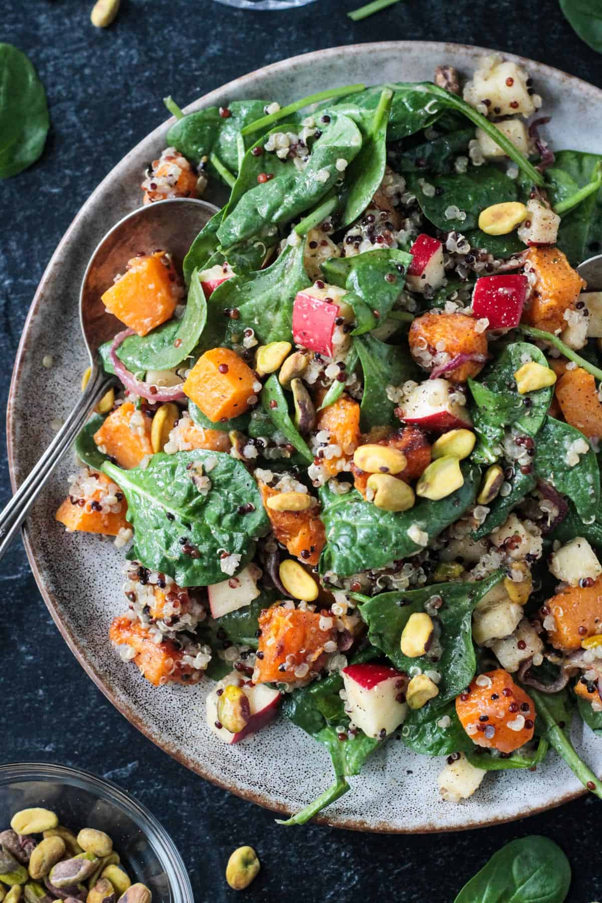 Cubes of roasted butternut squash on plate of baby spinach with quinoa, apples, and pistachios.