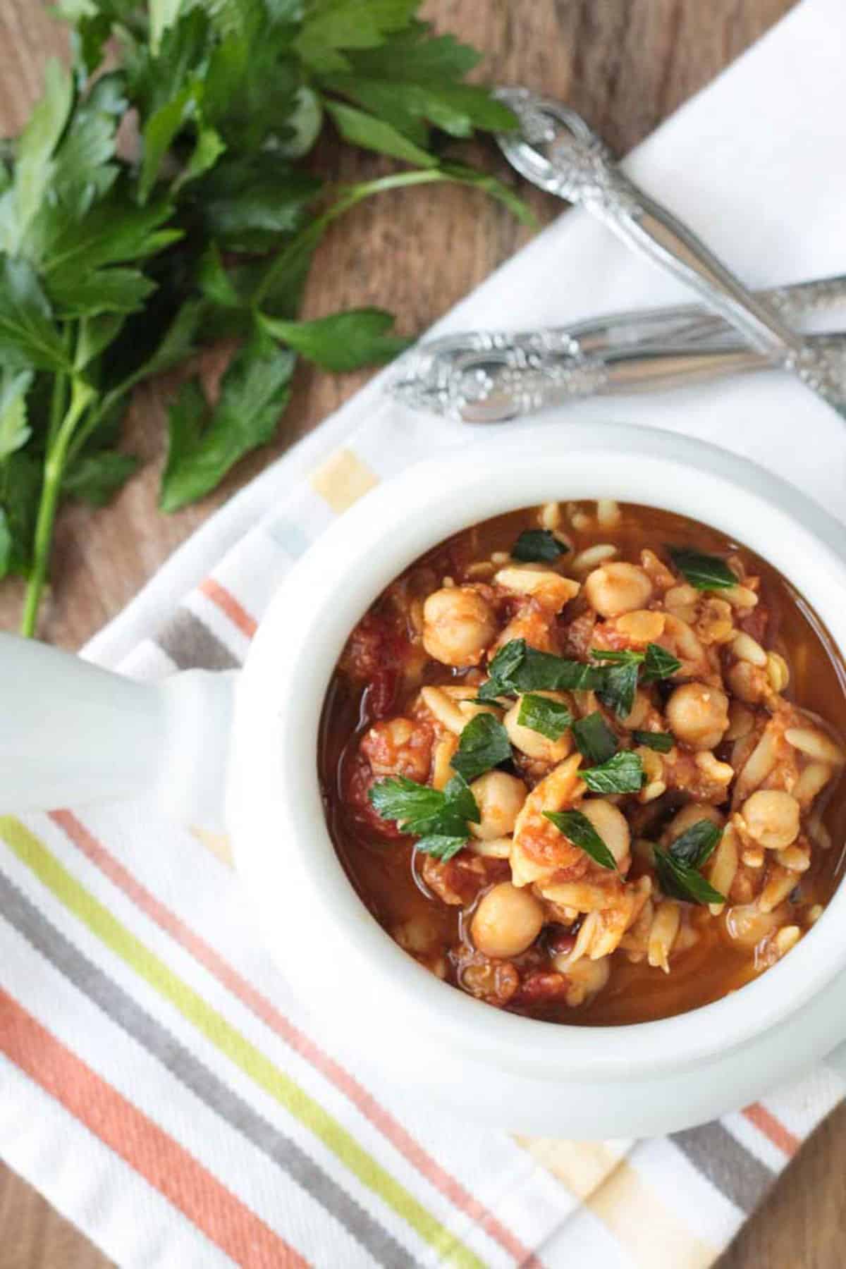 Bowl of soup on a striped dishcloth next to a bunch of fresh parsley.