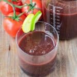 Glass of homemade spicy tomato juice garnished with a lime and lemon slice.