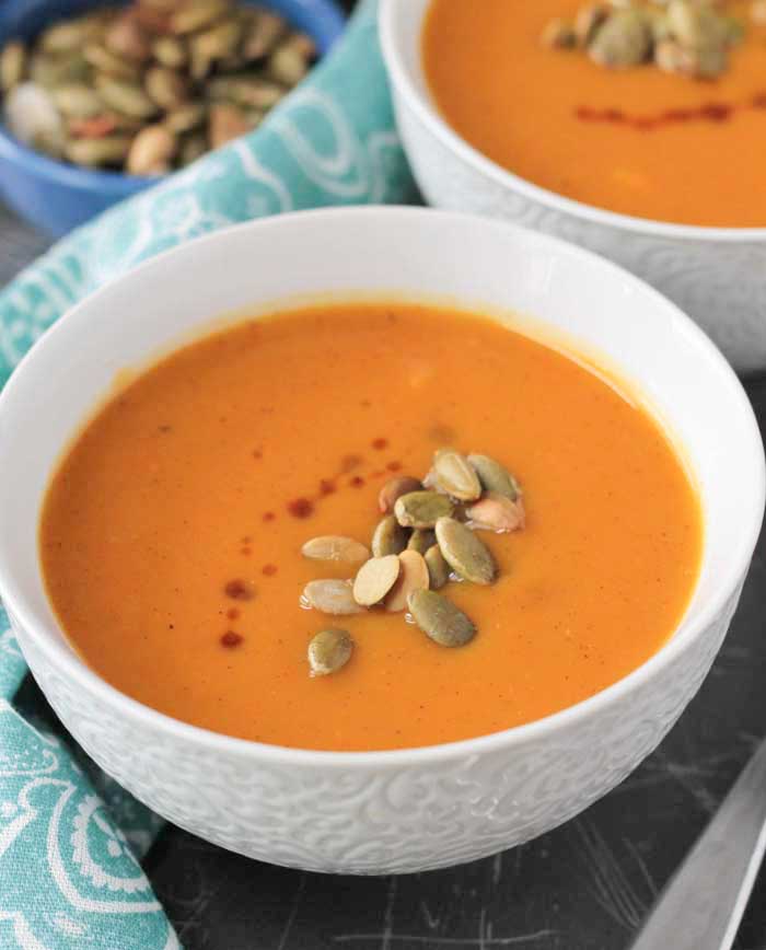 Butternut Squash Apple Soup in a white bowl. Roasted pumpkin seeds sprinkled on top. 