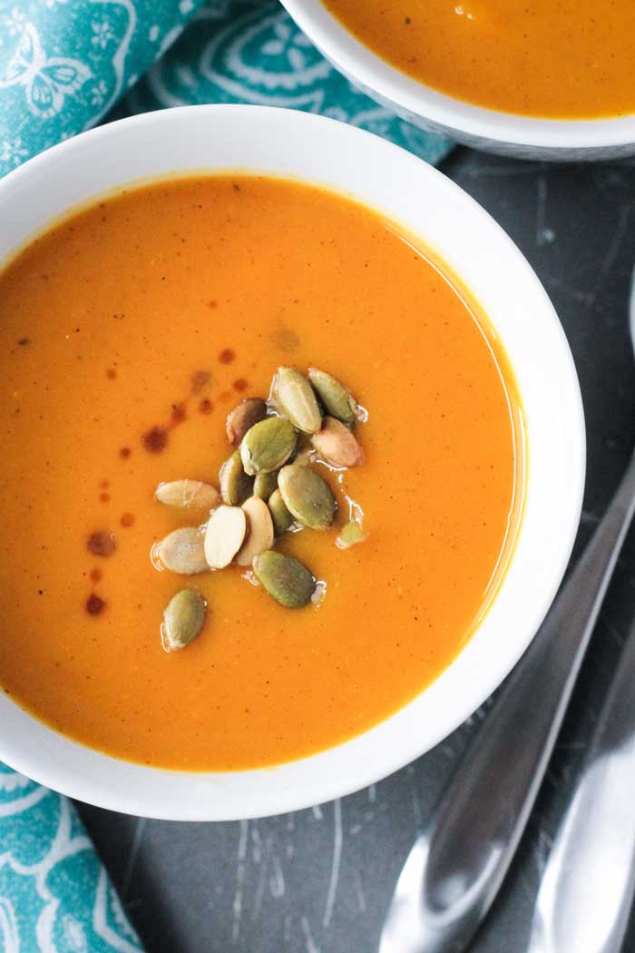 Bowl of Butternut Squash Apple Soup topped with roasted pumpkin seeds and a few splashes of balsamic vinegar. 