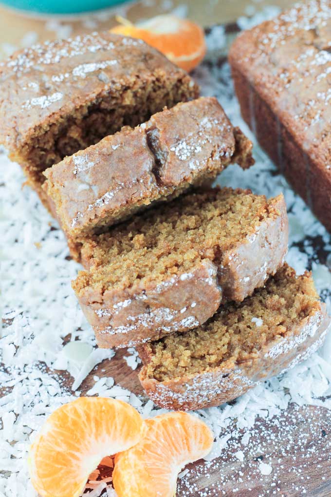 A sliced Coconut Clementine Mini Loaf Cake surrounded by shredded coconut and clementine segments.