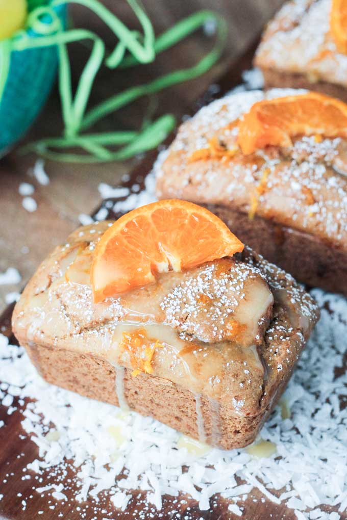 Coconut Clementine Mini Loaf Cakes on a wooden board surrounded by shredded coconut.