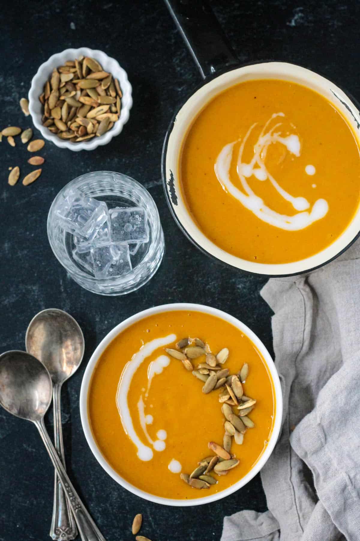 Two bowls of soup next to a glass of water and a small bowl of pumpkin seeds.