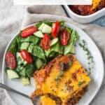 Slice of lentil shepherd's pie on a plate with a side of salad.