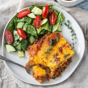 Slice of lentil shepherd's pie on a plate with a side of salad.
