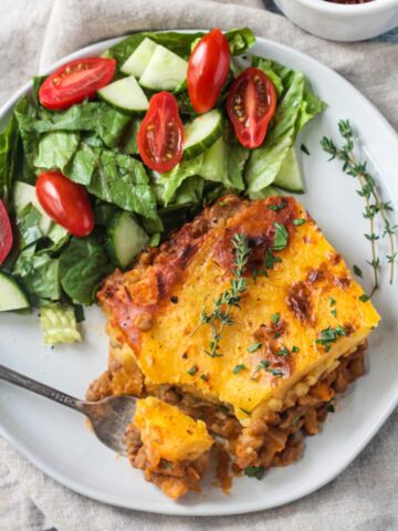 Slice of lentil shepherd's pie on a plate with a side of salad.