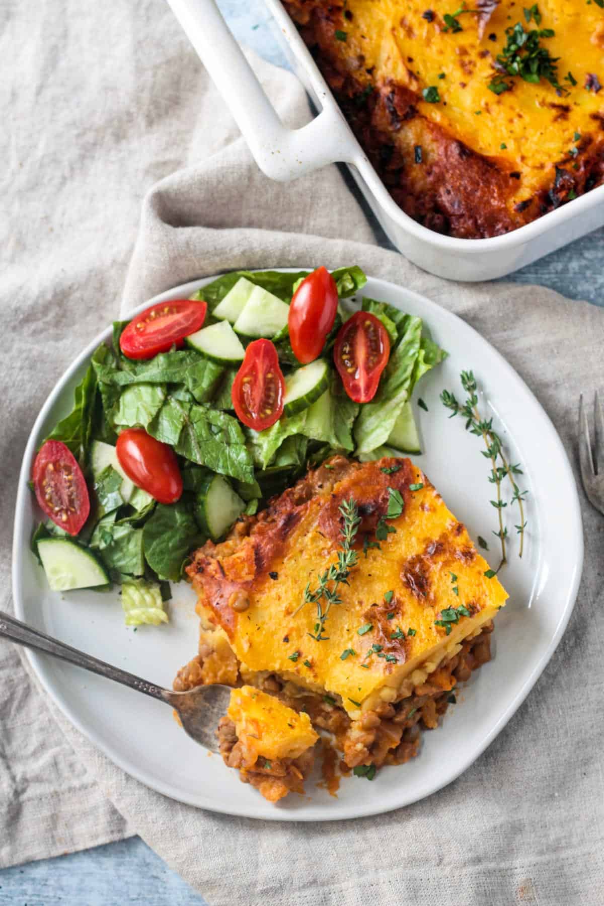 Vegetarian Cottage Pie with lentils, winter squash, cauliflower and spices in a rich savory tomato sauce and topped off with creamy carrot mashed potatoes. A delicious meatless comfort food recipe the whole family will love! Slice of lentil shepherd's pie on a plate with a side of salad.