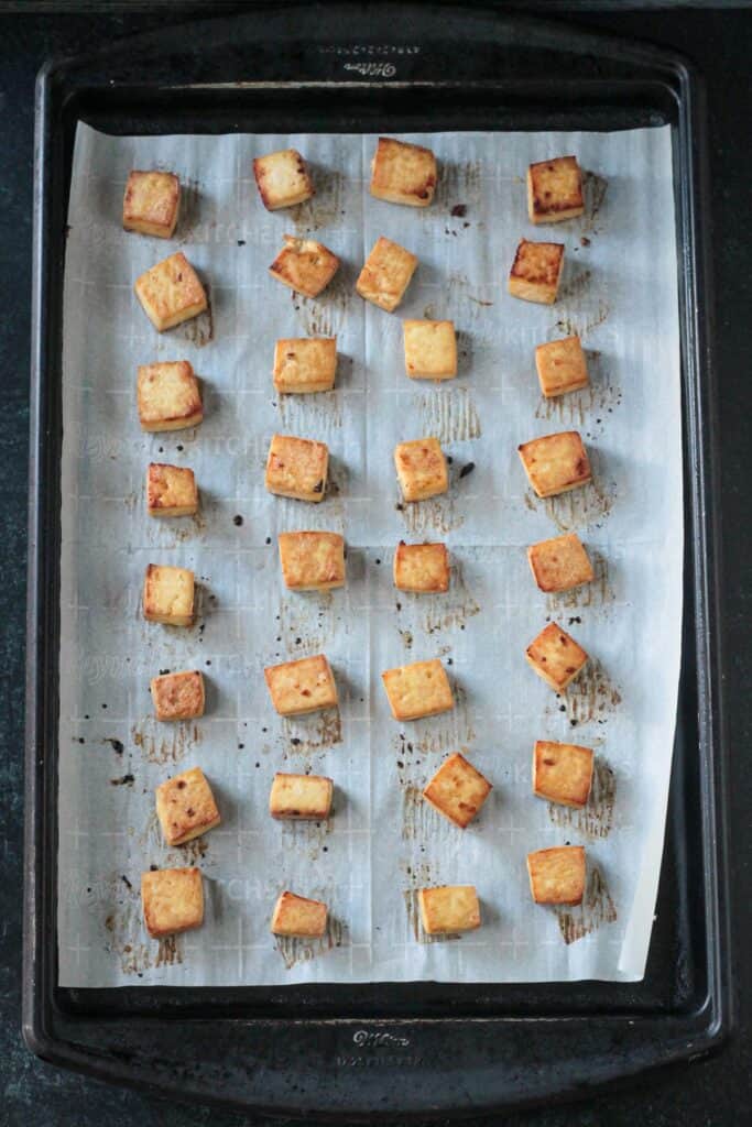 Baked tofu cubes on a parchment lined baking sheet.
