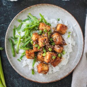 Baked sesame ginger tofu plated over rice with a side of green beans.