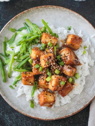 Baked sesame ginger tofu plated over rice with a side of green beans.