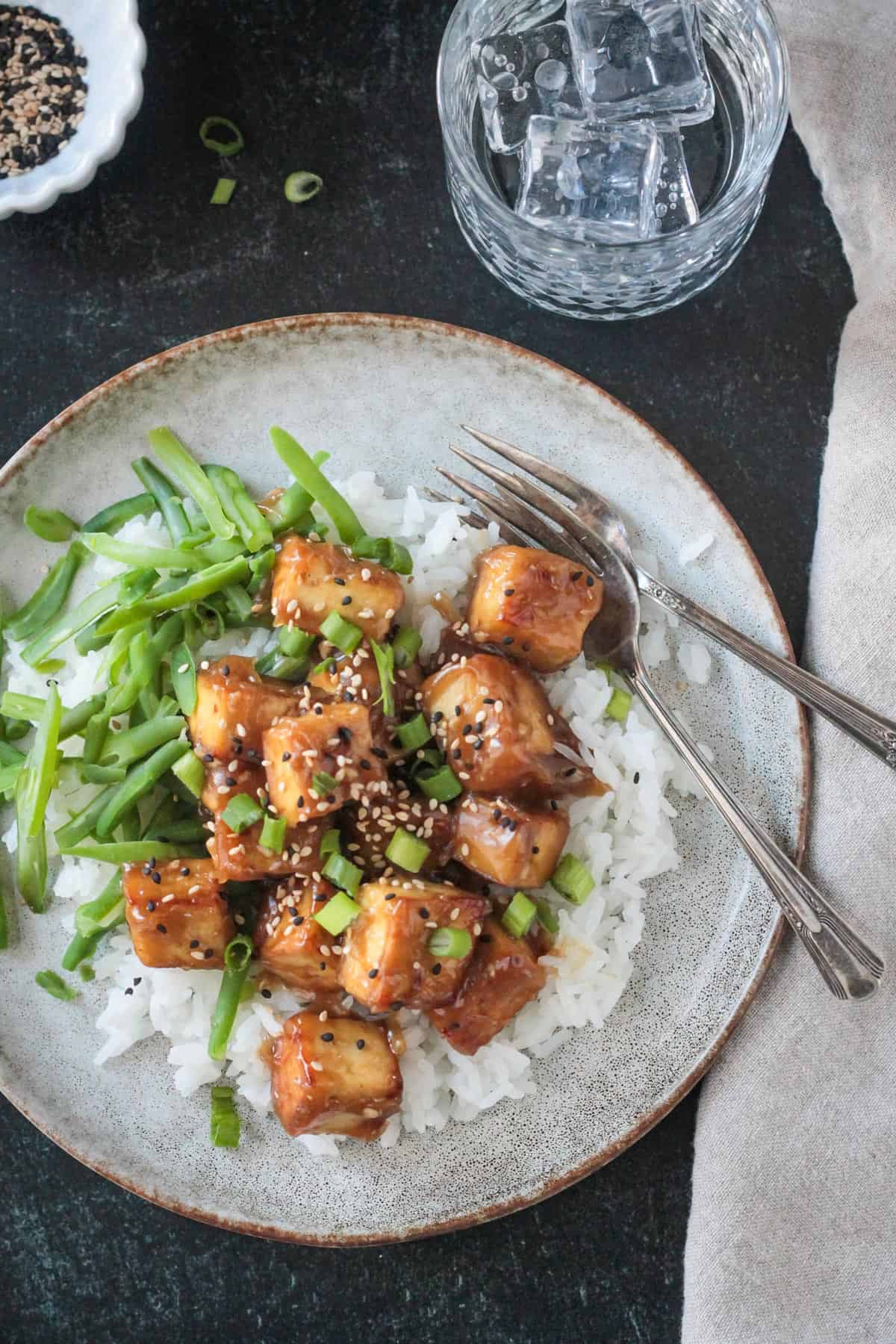Sesame ginger tofu over rice with two forks on a plate.