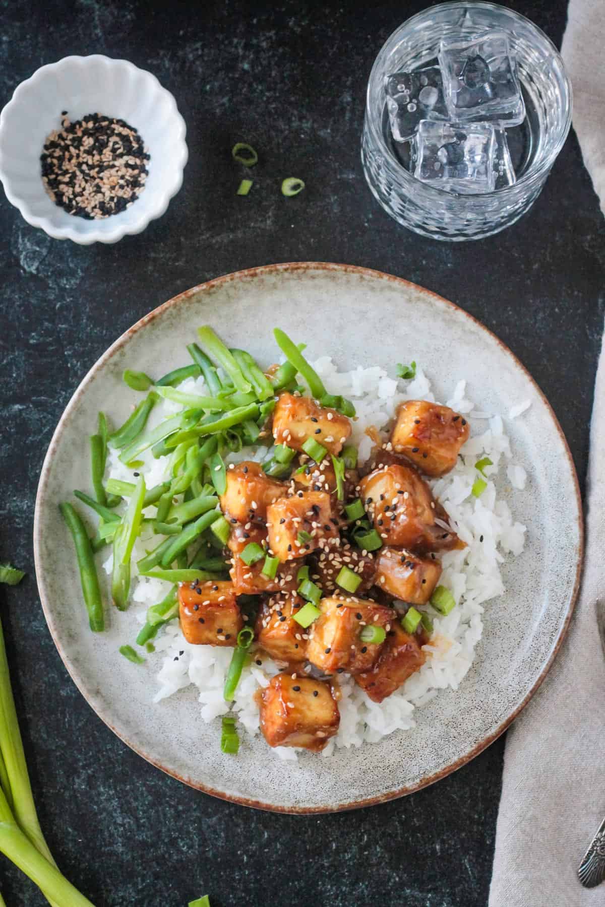 Baked sesame ginger tofu plated over rice with a side of green beans.