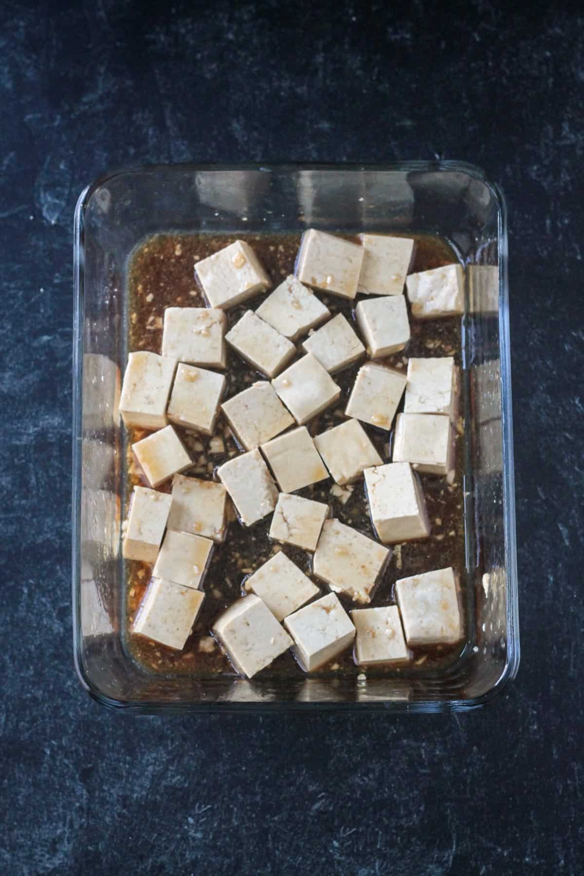 Cubes of tofu in a glass container with marinade.