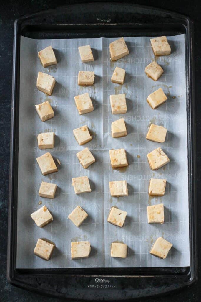 Marinated cubes of tofu on a parchment lined baking sheet.