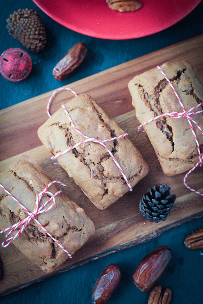 3 mini date nut loaves wrapped in red/white twine on a wooden board.