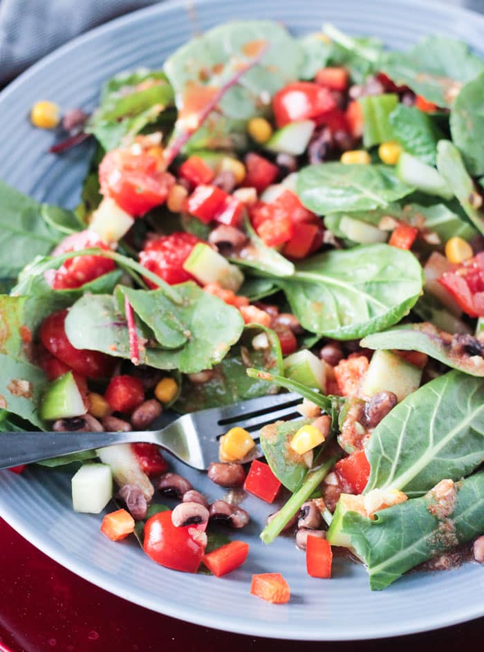 A fork stabs a bite of food from a plate of baby greens salad with black eyed peas and veggies.