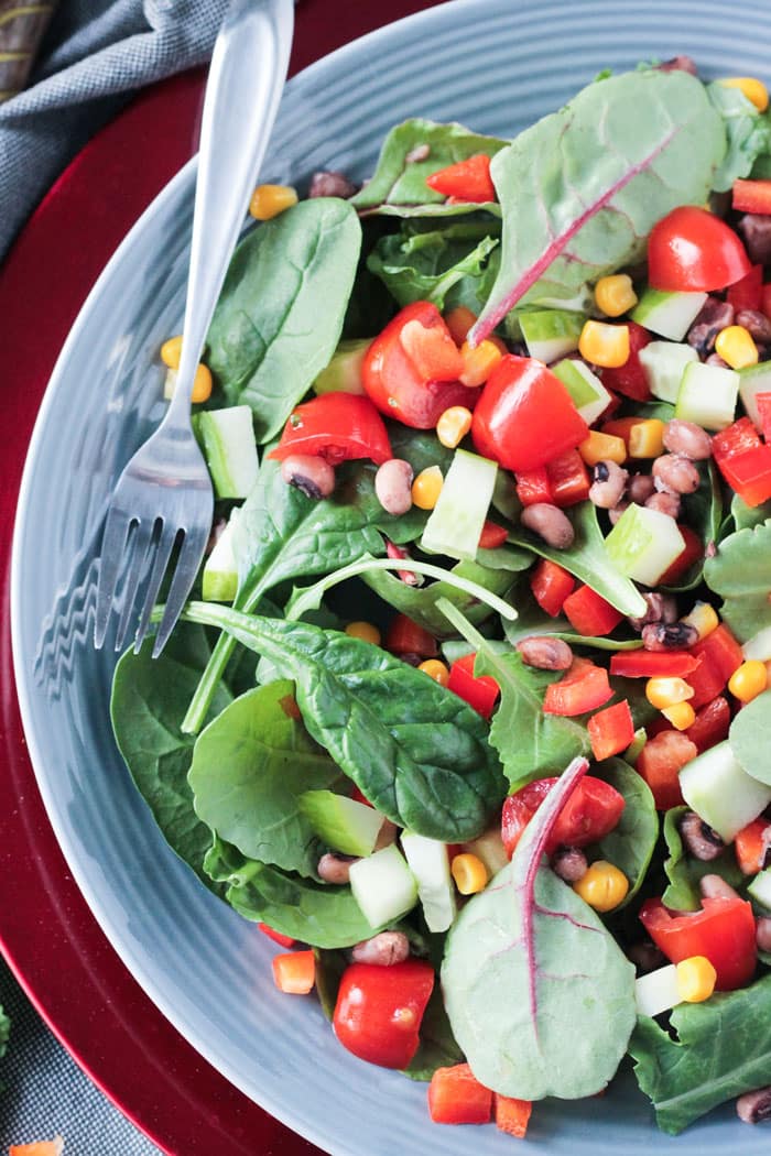 Overhead view of a salad of baby spinach, baby kale, cherry tomatoes, corn, black eyed peas, and red peppers.