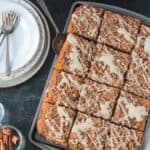 Sliced cinnamon streusel pumpkin coffee cake next to a stack of plates and forks.