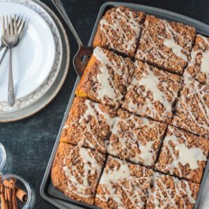 Sliced cinnamon streusel pumpkin coffee cake next to a stack of plates and forks.