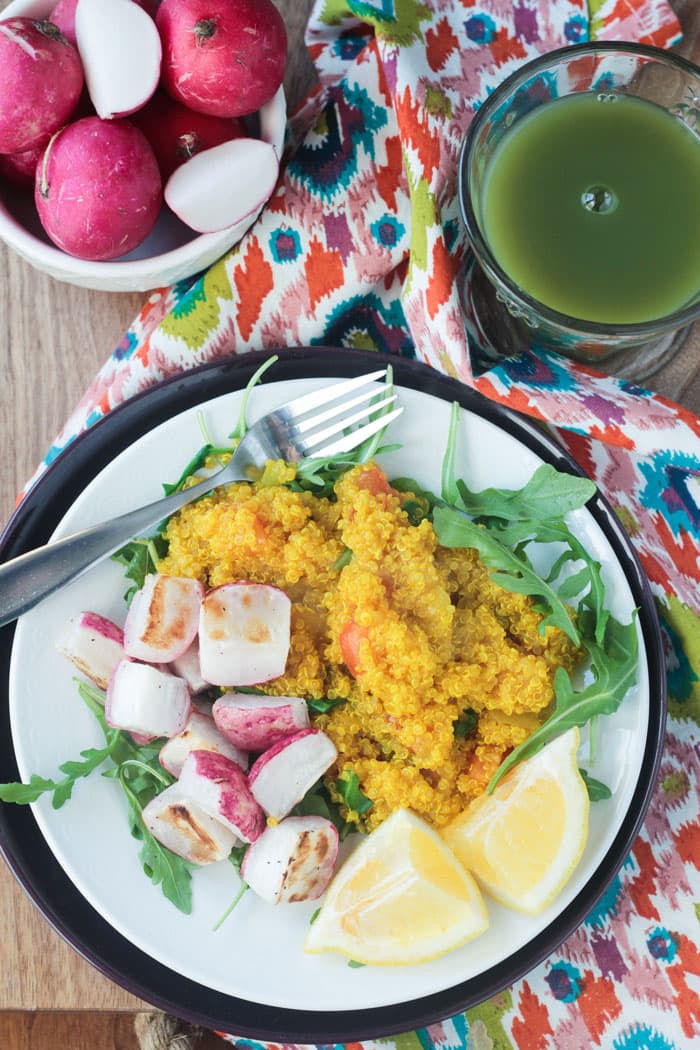 Quinoa Power Breakfast with arugula and roasted radishes - a protein packed, flavorful, nutritious way to start your day. And it can be made in just 30 minutes! Breakfast plate of turmeric quinoa, chopped roasted radishes, arugula, and two lemon wedges. Bowl of raw radishes behind next to a glass of green juice.