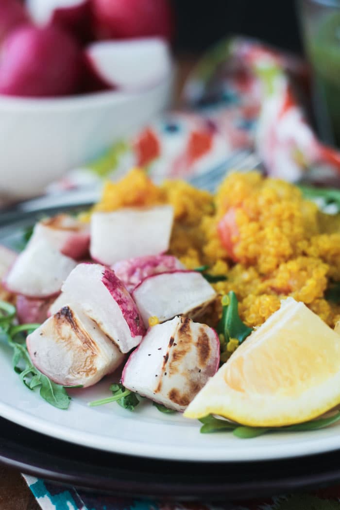 Roasted radishes with perfectly browned edges on a plate next to a lemon wedge and quinoa. 