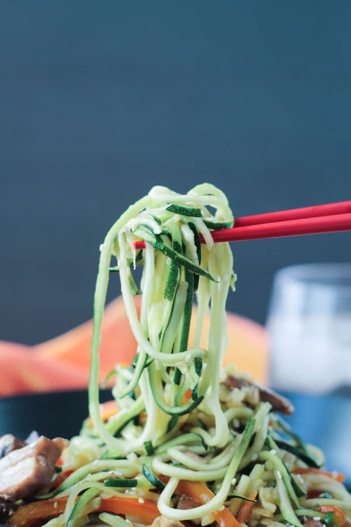 Red chopsticks lifting up a bite of zucchini noodles. 