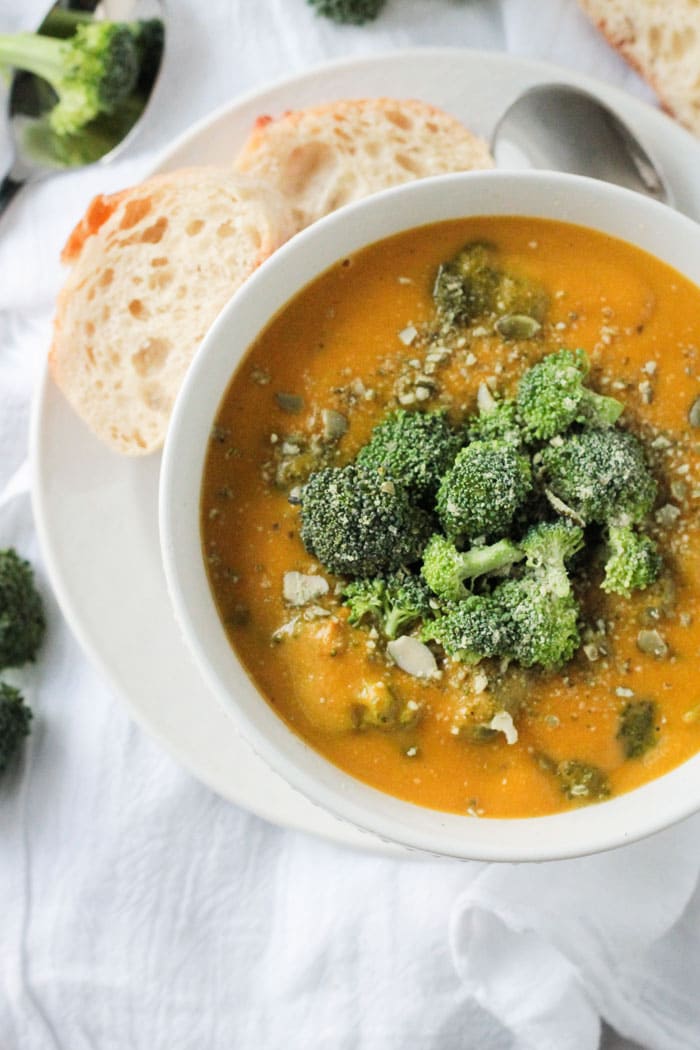 Bowl of Vegan Broccoli Cheese Soup with lots of broccoli florets on top. Sprinkled with crushed pumpkin seeds. Two slices of bread on the side.