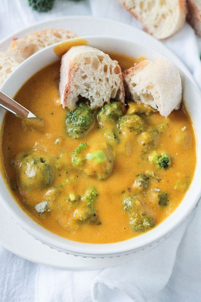 Bowl of Vegan Broccoli Cheese Soup. Metal spoon in the soup and one torn piece of crusty bread on the side.