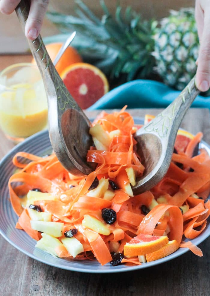 Wooden salad serving spoons picking up a serving of carrot pineapple salad from the serving dish.