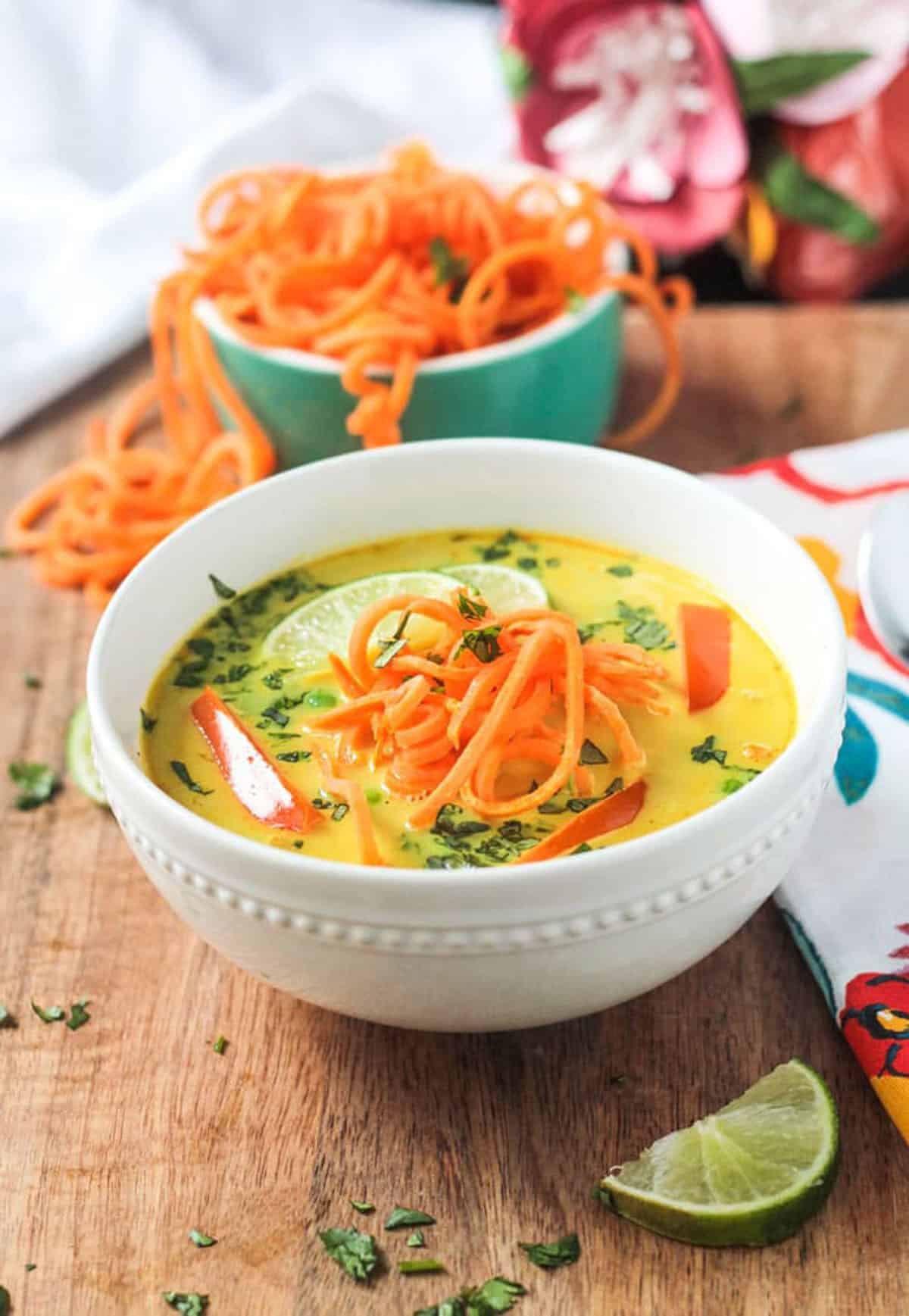 Spiralized sweet potato noodles spilling out of a bowl behind a bowl of soup.