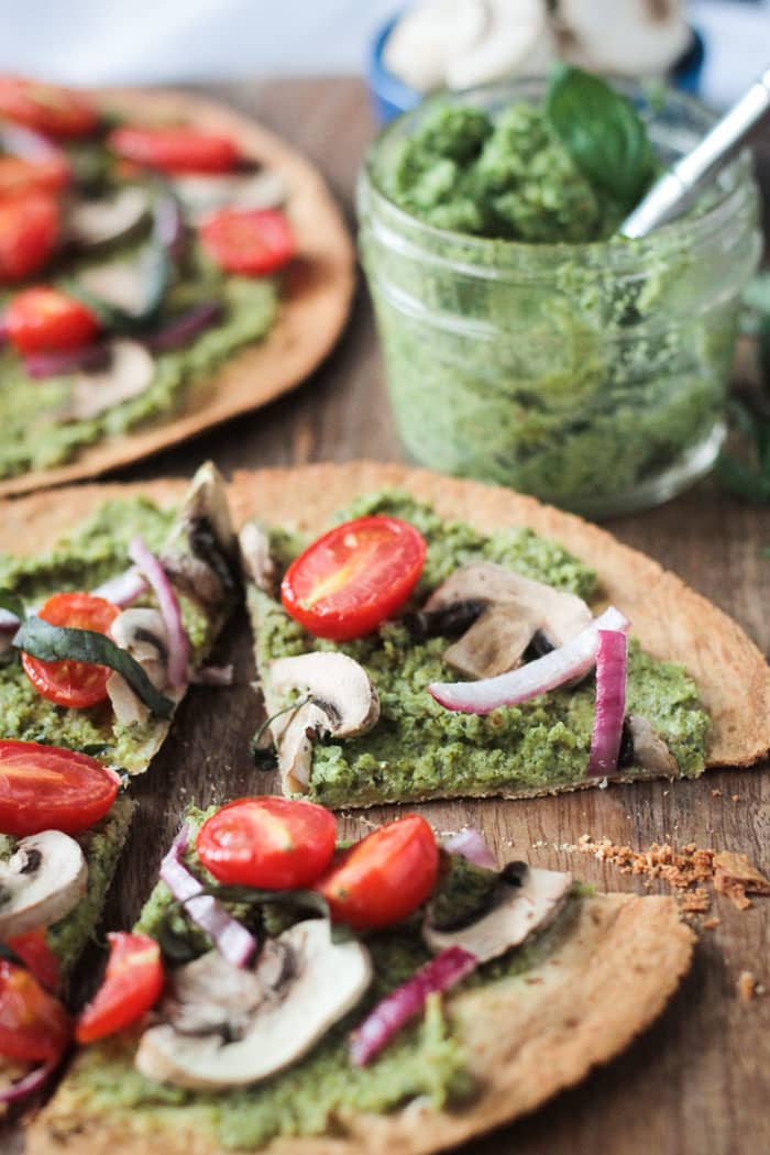 Easy Vegan Pesto Tortilla Pizza sliced into 4 slices. Small glass jar of pesto with a metal spoon in it behind.