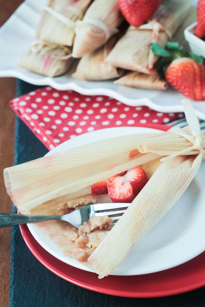 An unwrapped vegan strawberry dessert tamale on a plate. A fork taking a bite out of the filling. Fresh strawberries inside.