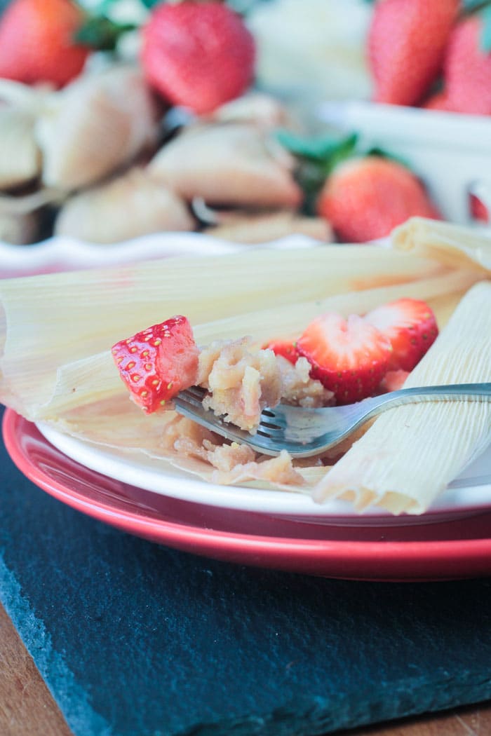 The inside of a vegan strawberry dessert tamale. A bite of the tamale with a piece of fresh strawberry on a fork. 