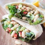 Two pita pockets stacked on top of each other and stuffed with White Bean Salad w/ cucumbers, red peppers, and red leaf lettuce.