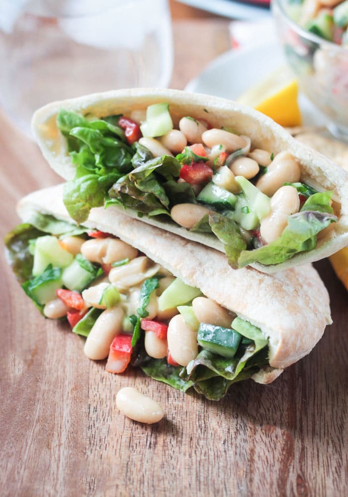 Two pita pockets stacked on top of each other and stuffed with White Bean Salad w/ cucumbers, red peppers, and red leaf lettuce.