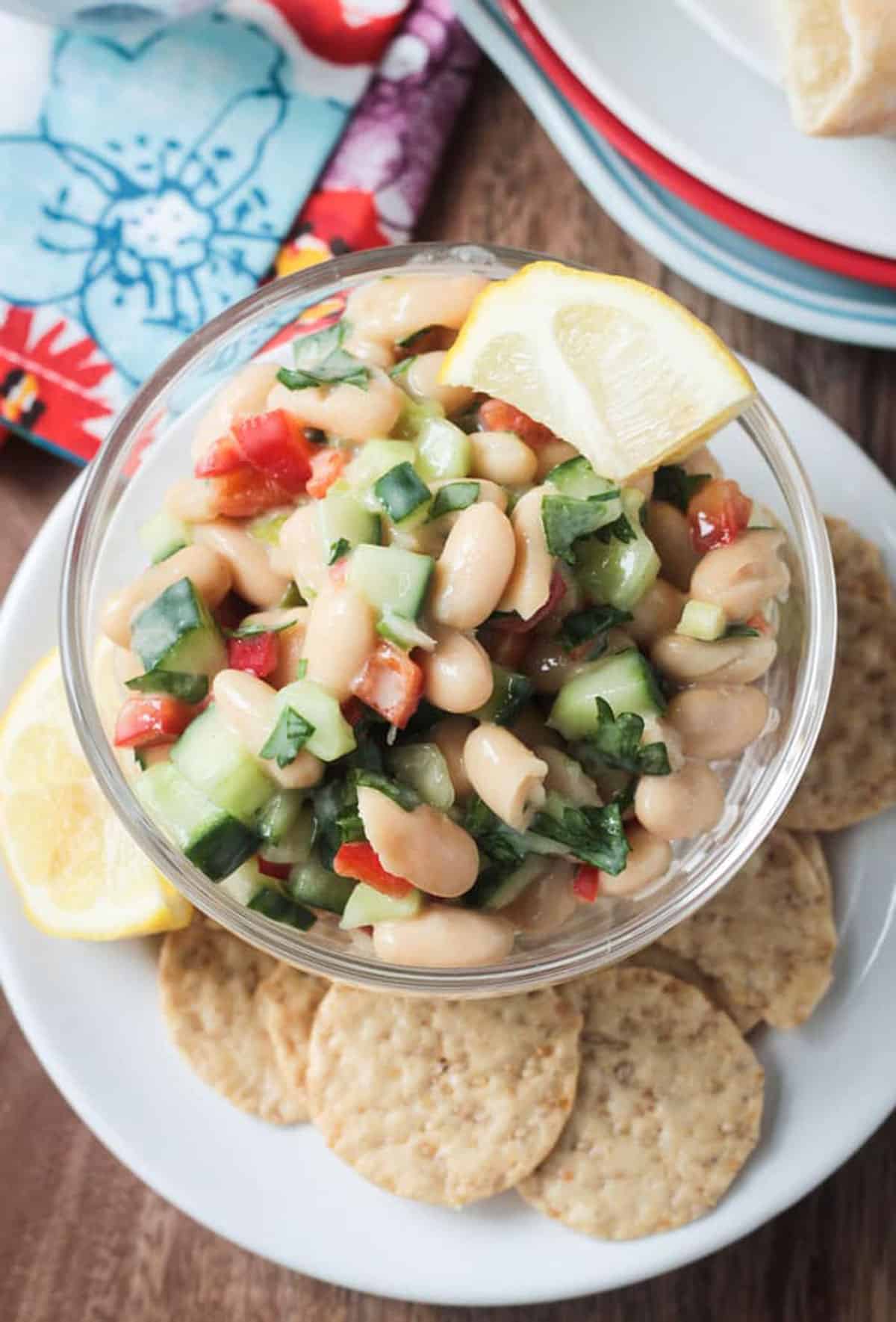 White bean salad in a bowl on a plate with crackers.