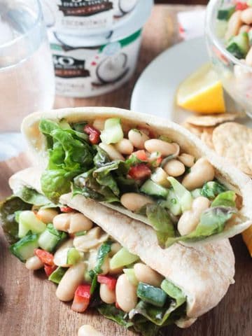 Two pita pockets filled with white bean salad stacked on a table.