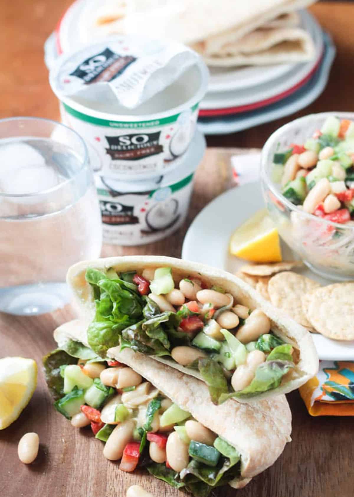 Two white bean salad pita pockets stacked in front of a yogurt container.