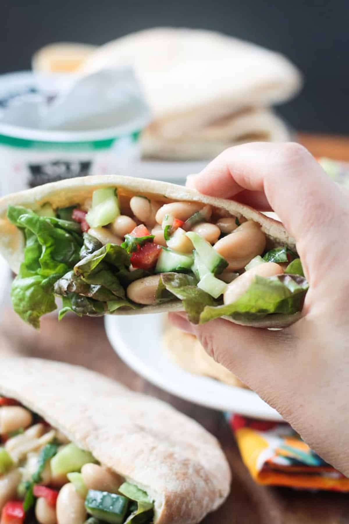 Hand holding a pita pocket filled with white bean salad.
