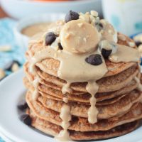 Stack of peanut butter pancakes topped with bananas, chocolate chips, and homemade maple peanut butter syrup dripping down the sides.