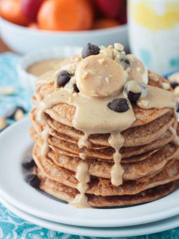 Stack of peanut butter pancakes topped with bananas, chocolate chips, and homemade maple peanut butter syrup dripping down the sides.