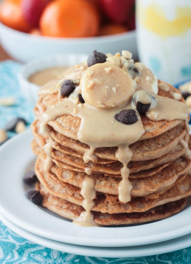 Stack of peanut butter pancakes topped with bananas, chocolate chips, and homemade maple peanut butter syrup dripping down the sides.